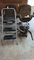 Image showing Shop-Vac vacuum and three-step ladder with swivel chairs in the background.
