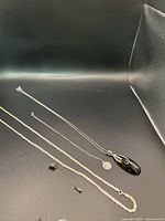 Full view of four silver chains and one small pin displayed on a black surface.