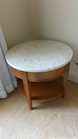 Full view of round wooden accent table with removable white marble top, situated on carpet.