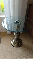 Full view of round glass top and brass base with filigreed, floral design and swirl pattern.