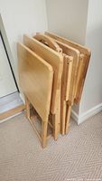 Four wooden tray tables stacked together with foldable stands visible, showing condition and size.