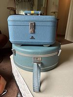Photo showing stacked blue McBrine train case on top of blue round Samsonite Silhouette case, illustrating shape, color, and hardware details.