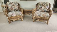 Two rattan wicker armchairs flanking matching side table with beveled glass top