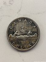 Front side of the 1957 Canadian Silver Dollar showing the canoe design with three men paddling, surrounded by the text 'CANADA DOLLAR 1957', showing wear and tarnish.