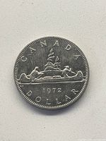 Obverse sides of the 1972 Canadian silver dollar coin showing two people canoeing with detailed background and inscriptions.