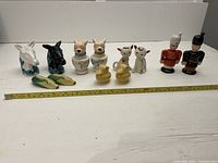 Full set of assorted vintage salt and pepper shakers displayed in one row with measuring tape along front showing scale.