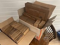 Photo showing multiple sizes of flat packed cardboard boxes mostly organized inside an open box on a table. Some boxes have numbered markings and tape.