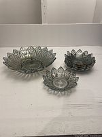Front view of one large and five small black carnival glass bowls arranged on white surface, showing the petal-shaped edges and iridescent finish.