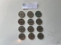 12 Buffalo nickels dated 1936 arranged in rows on a white surface with a handwritten '1936' label above them
