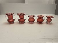 Set of 5 cranberry glass bud vases in a row from tallest to shortest, showing overall size and uniform color.