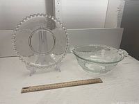 Photo of clear glass serving plate with scalloped beaded rim and etched floral design, displayed upright with ruler for scale.