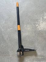 Full length view of Fiskars weed puller, showing black handle with orange accents and metal prongs at the base.