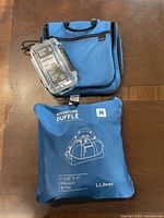 Photo showing three items: Maximum water-resistant storage case (clear), blue organizational travel bag with handles, and blue L.L. Bean Adventure Duffle bag packed in its pouch.