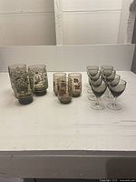 Set of 14 MCM glassware pieces including three tall tawny glasses with black daisies, three short tawny glasses with red flowers, and eight black stemmed shot glasses.