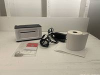 Munbyn shipping label printer with a partial roll of thermal labels, power adapter, and USB setup key with instructions on a white surface.