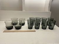 Both sets of smokey glasses shown together with a ruler for scale. Set 1: 4 shorter, wider glasses. Set 2: 8 taller, narrower glasses.