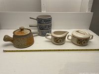 Photo of all items together including the French onion soup bowl with lid and handle, stacked chili bowls with blue lettering, and floral cream and sugar set, with measuring tape showing sizes.