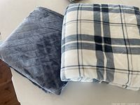 Two folded blankets, one solid navy blue with diamond pattern, one blue and white plaid.