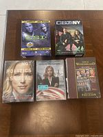 Top-down photo of all 5 DVD box sets arranged on a wooden surface, showing front covers clearly.