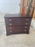 Front view of dark wood filling cabinet showing four drawers and brass handles.