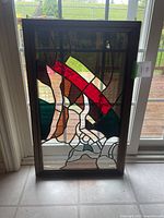 Full view of stained glass panel backlit by window, showing abstract geometric design with red, green, brown, white, and clear glass sections.