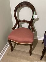 Full view of antique carved wood chair with dusty rose fabric seat and dark wood frame.