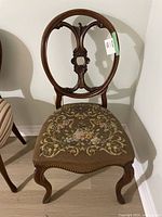 Front view of carved wood chair with oval backrest and floral embroidered cushioned seat.