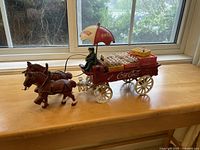 Side view of the Coca-Cola horse drawn wagon with brown horses, red wagon body, Coca-Cola umbrella, and loaded with miniature glass bottles in crates.