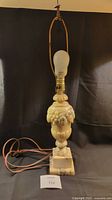 Front view of alabaster lamp base standing with bulb installed and attached metal harp for a lampshade.