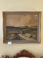 Full view of framed landscape painting with road, buildings, and hills.