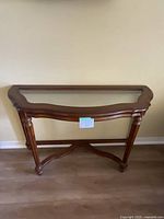 Full view of wood hall console table with glass inset top, showing structure and decorative apron.