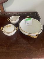 Full view of the cream pitcher, sugar bowl with lid, and serving bowl on a wooden surface.