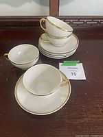 Four white porcelain teacups stacked with five saucers beneath, placed on a wooden surface.
