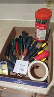 Photo of the lot showing multiple screwdrivers of different colors and sizes, a container with black zip ties, a roll of white tape, and some packaging with blades.