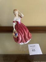 Full view of the Paragon Spring figurine showing the woman in red dress holding floral hat