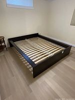 Full view of assembled queen bed frame with wooden slats in a room with a beige floor and white walls.