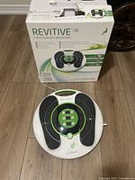 Revitive IX Circulation Booster device placed on the floor with original box behind it, showing device top view and condition.