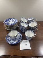 Overall photo of 10 blue and white Royal Crown Derby teacups and 12 matching saucers arranged on table