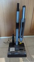 Front view of Shark PowerFins cordless vacuum with dock and handheld accessories on floor against wooden door.