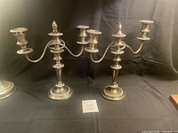 Full view of both silver candelabras side by side on a black surface showing their overall size and shape.