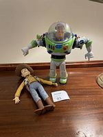 Buzz Lightyear and Woody dolls shown on wooden surface with numbered lot marker.
