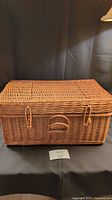 Front view of rectangular wicker picnic basket with closed lid, showing latch closures and handle.