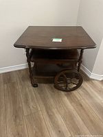 Full view of the antique wooden tea cart showing its square tabletop, turned legs, and large spoked wheels.
