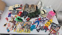 Overview of entire lot on table showing many vintage toys including Ecto-1 vehicle, Space Force figures, wrestling and superhero figures, and others.