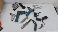 Overview of all tools on white table including Makita drill and various handheld power and air tools