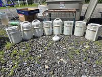 Eight Lusterware canisters with lids and one extra lid arranged on gravel outdoors, showing iridescent finish and wear.