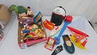 Overview of vintage toys lot including a red die-cast car carrier, plastic boats, a turtle, small toy figures, and accessories arranged on a white surface