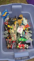 Top view of large blue tote filled with mixed action figures and toys, assorted colors and types visible.