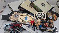 Overview showing wrestling figures, belts and WWE toy ring with some accessories and cables.