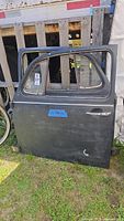Single black exterior door with VW glass, standing upright outdoors on grass with wooden pallet background.